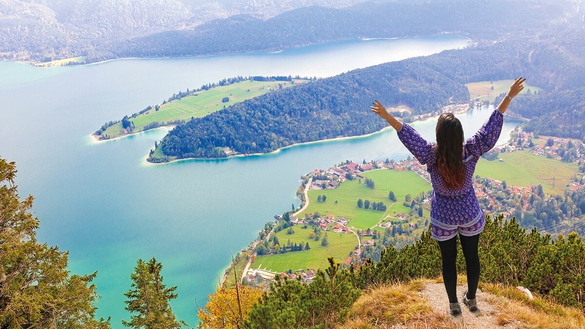 Junges Mädchen steht auf einem Berg und schaut hinab auf die grüne Landschaft