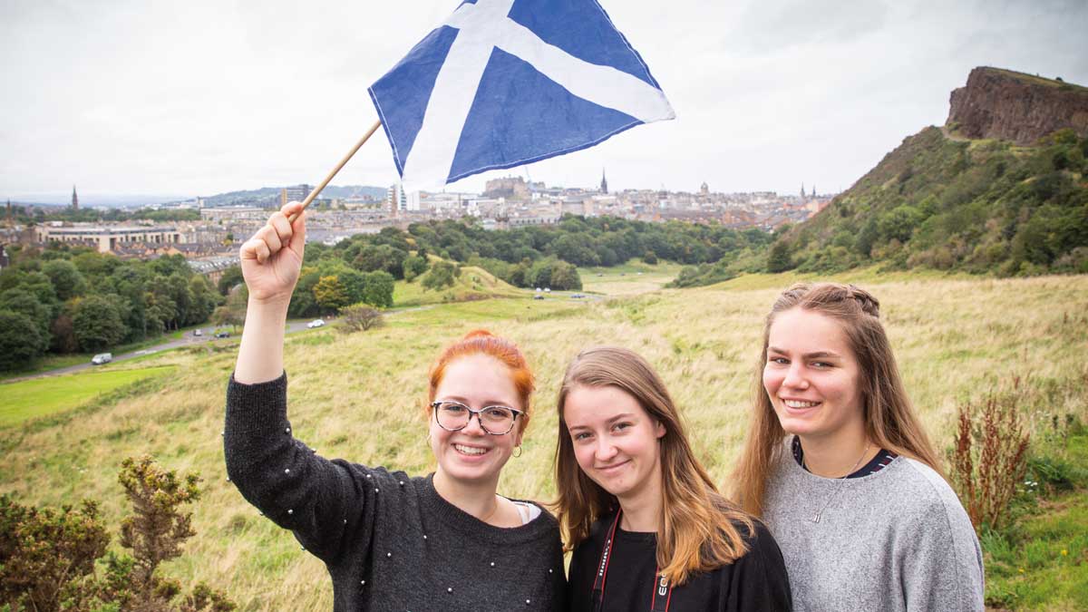 Drei Schülerinnen stehen auf einer Wiese und halten eine Schottland Fahne in der Hand
