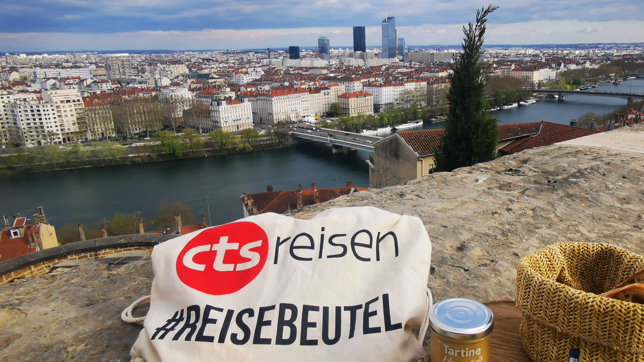 Sicht auf Lyon mit CTS Reisebeutel und französischen Speisen im Vordergrund