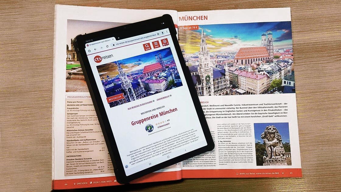 Unsere Katalogseite mit dem Reiseziel München aufgeschlagen neben einem Tablet, auf dem das gleiche Reiseziel im Internet aufgerufen ist.