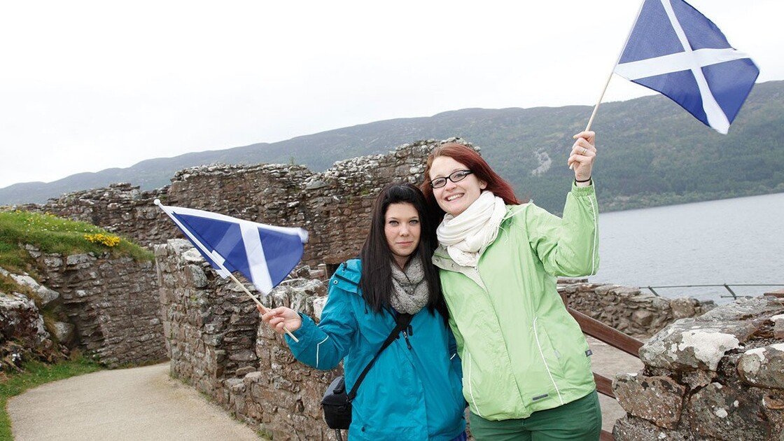 Zwei Schülerinnen beim Urquhart Castle in Schottland mit Flaggen in der Hand